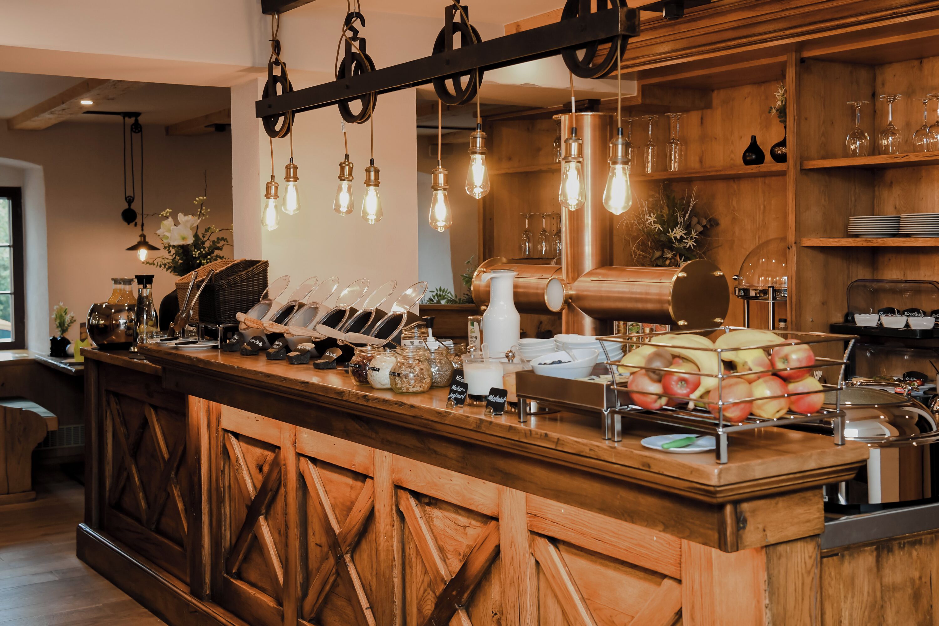 Mostrador de madera con diseño rústico, que presenta una máquina de café, una exposición de frutas y lámparas colgantes.