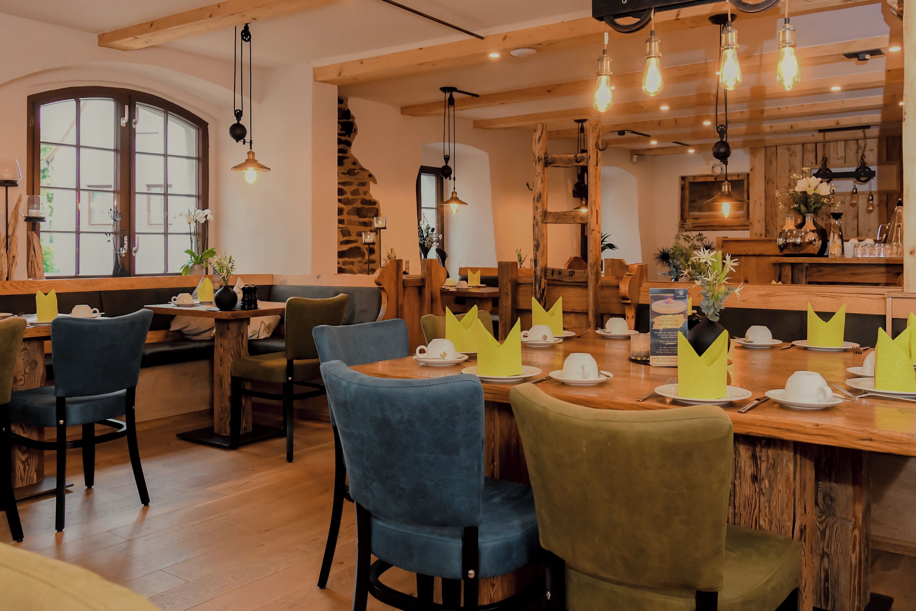 A cozy restaurant with wooden tables and chairs, a stone wall, and hanging light fixtures.