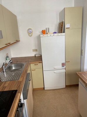 A compact kitchen with a sink, stove, and a white refrigerator. - 2-room apartment in green setting near Rheinfelden-Adelhausen, terrace & garden (Rheinfelden)