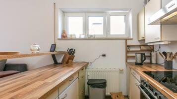 Une cuisine compacte avec une fenêtre, des plans de travail en bois, une bouilloire et une poubelle.