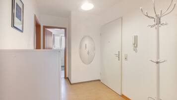Un couloir avec une porte blanche, un porte-manteau, un tableau encadré et un luminaire.
