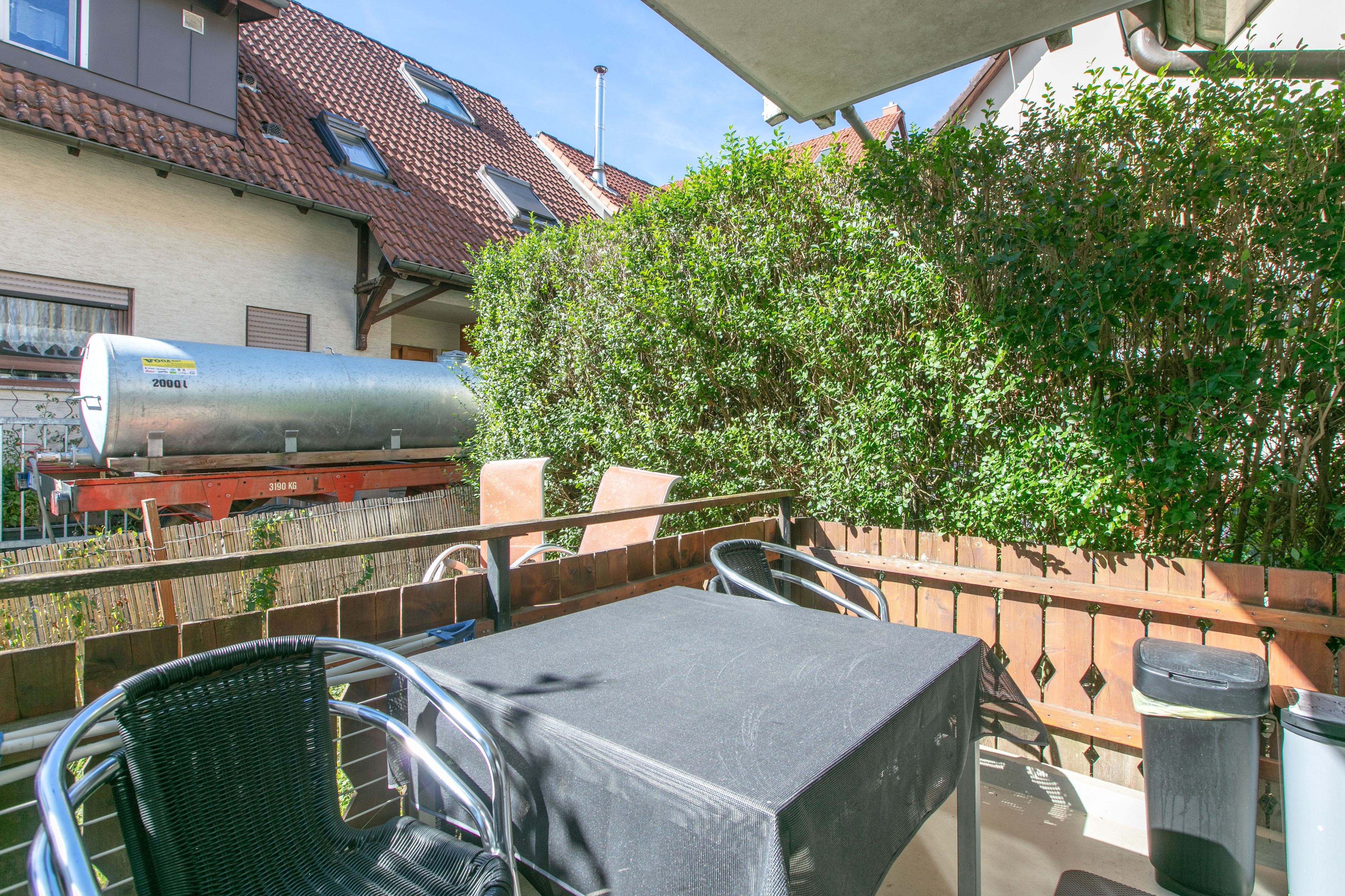 Eine Außenpatio mit Tisch und Stühlen, einem Metalltank und einem Holzzaun.