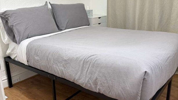 A single bed with a grey mattress and pillows, a wooden floor, and a white wall. - Relocate to the Loop • Quiet 2BR near WashU 1N (University City)