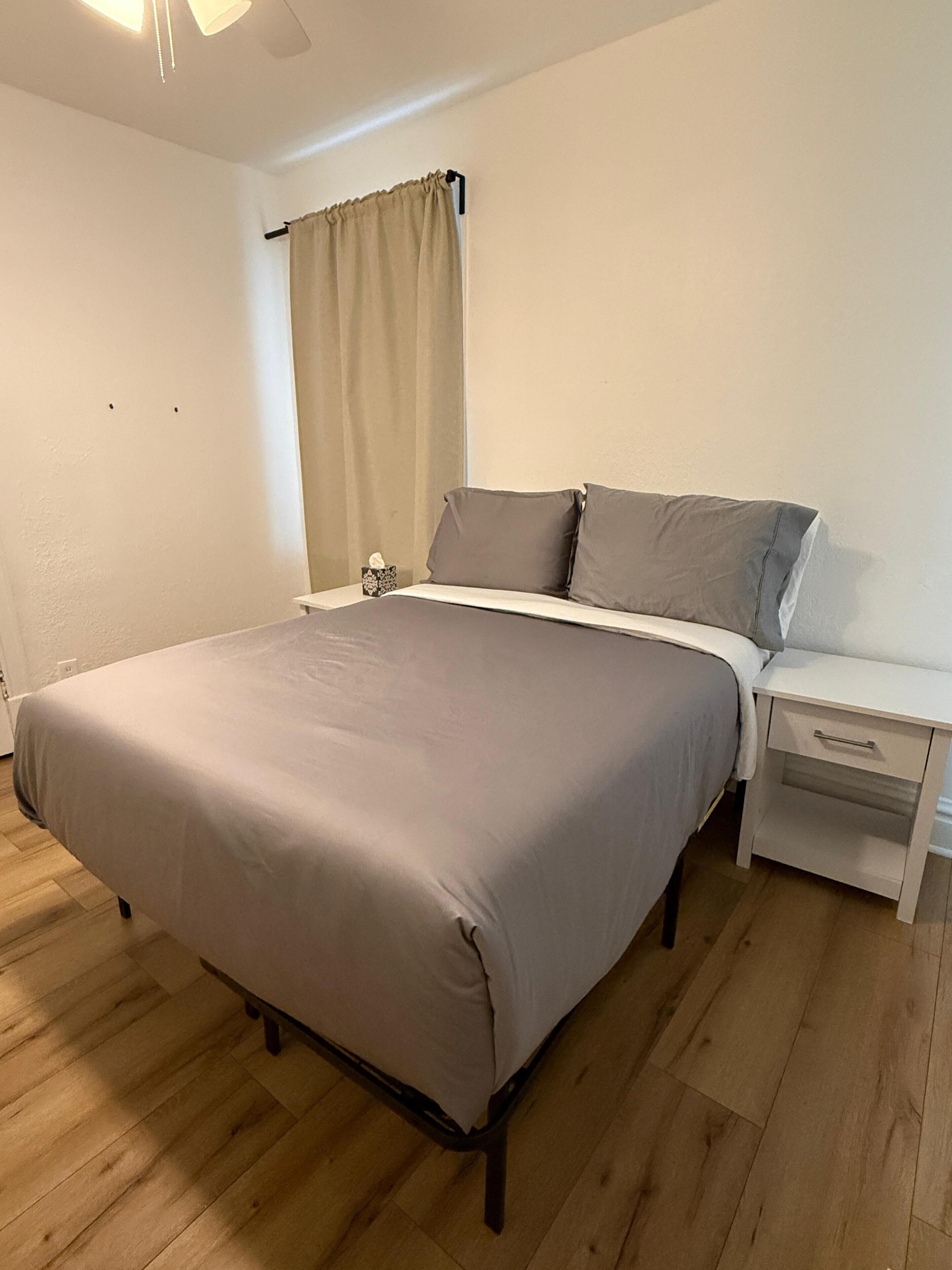 A bedroom with a bed, nightstand, and a window with curtains.
