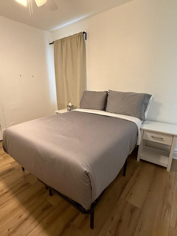 A bedroom with a bed, nightstand, and a window with curtains.