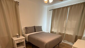 A bedroom with a bed, bedside table, nightstand, ceiling fan, and large windows with curtains. - Relocate to the Loop • Quiet 2BR near WashU 1N (University City)