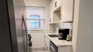 A compact kitchen with a stainless steel refrigerator, a window with blinds, a sink with a faucet, and a countertop with a coffee maker. - Relocate to the Loop • Quiet 2BR near WashU 1N (University City)
