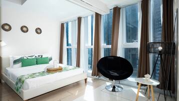 Une chambre d’hôtel moderne avec un grand lit, une chaise noire, une petite table et une vue sur la ville grâce à de grandes fenêtres.