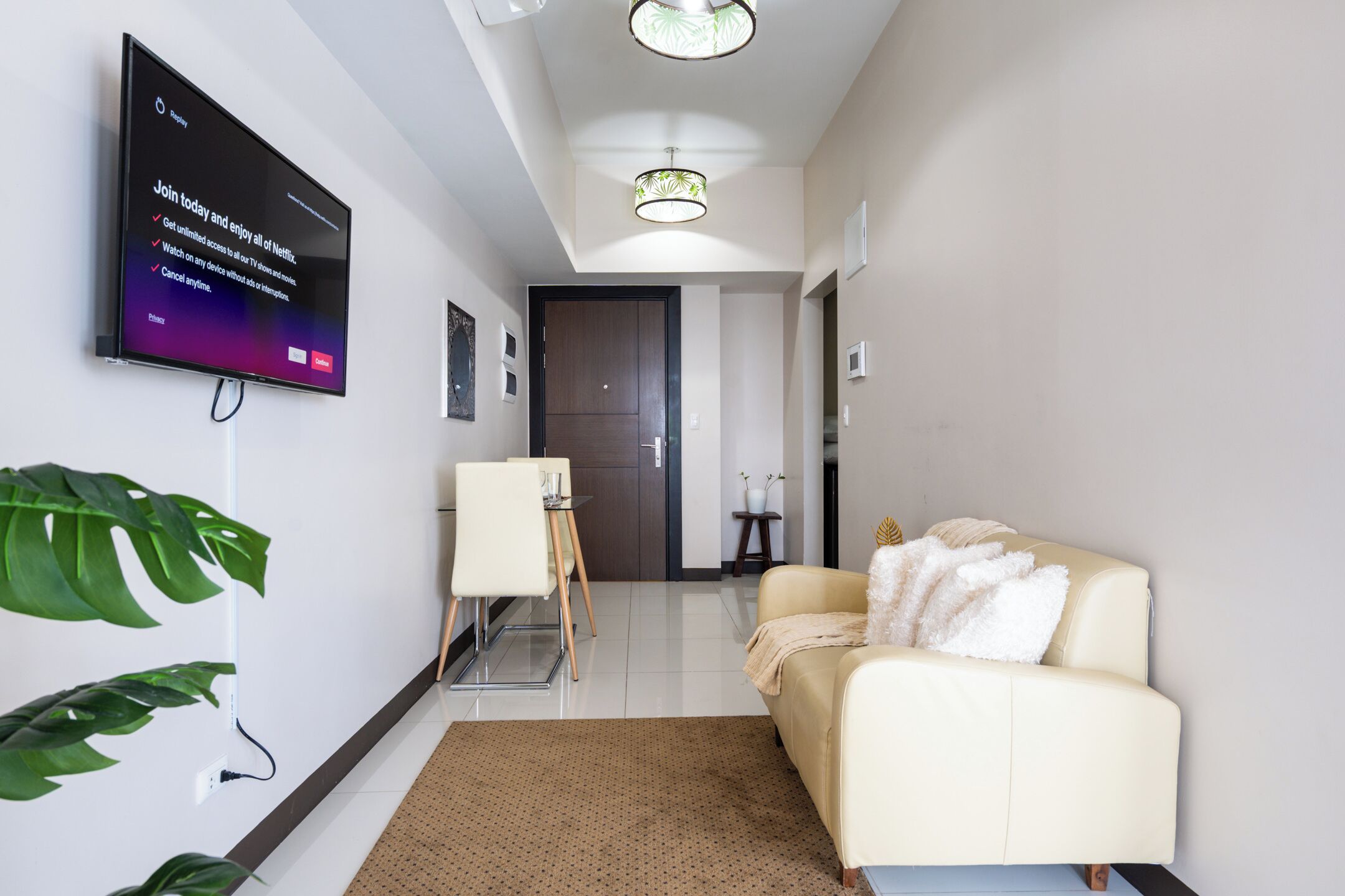 Un salon moderne avec un téléviseur à écran plat fixé au mur, un canapé, une table basse et une petite table avec une chaise.