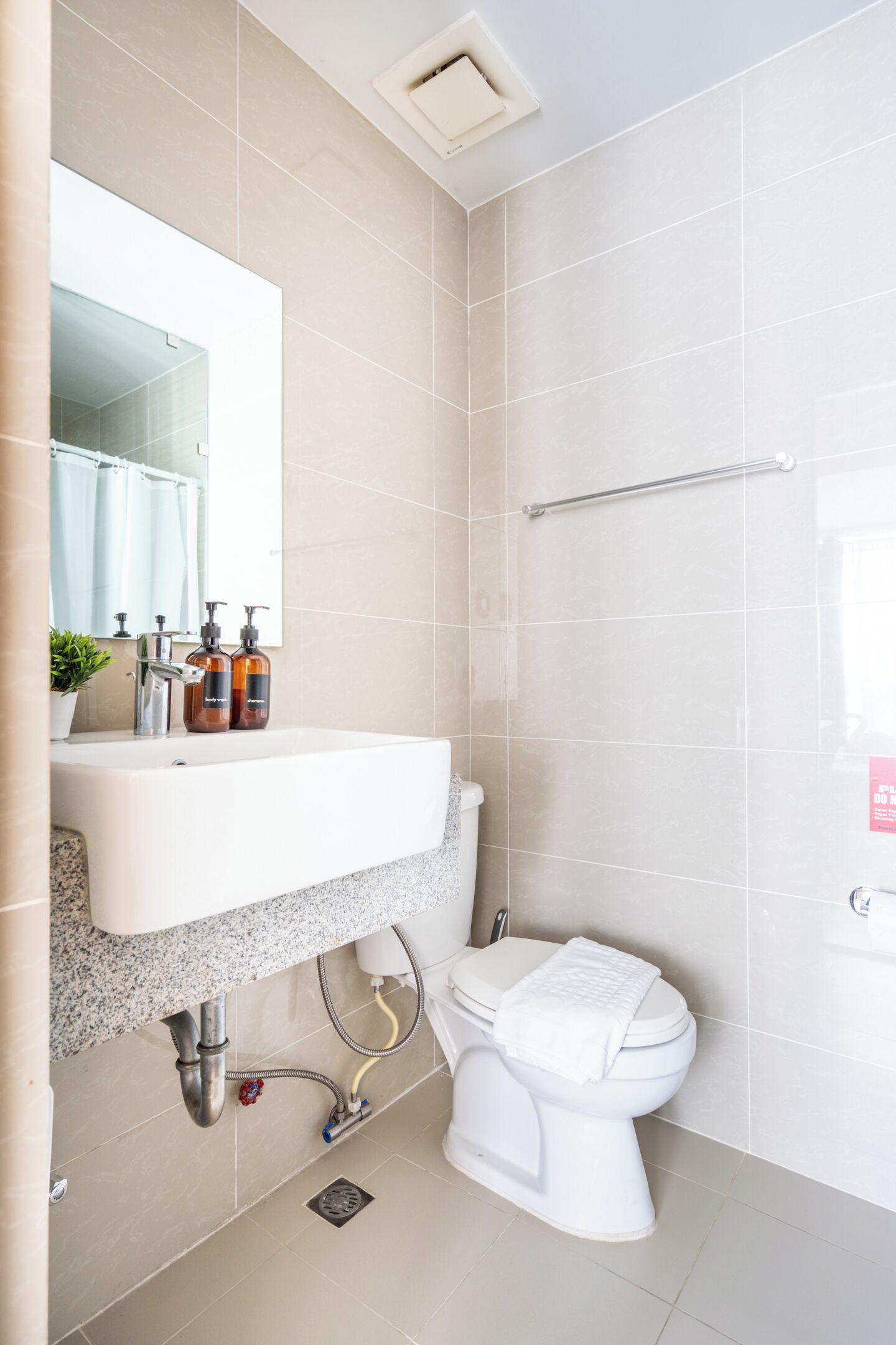 Une salle de bain moderne avec un lavabo blanc, un miroir et des toilettes. On trouve des articles de toilette sur le lavabo et une serviette sur les toilettes.
