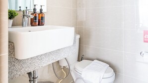 Een moderne badkamer met een wit wastafel, spiegel en toilet. Er staan toiletartikelen op de wastafel en een handdoek op het toilet.