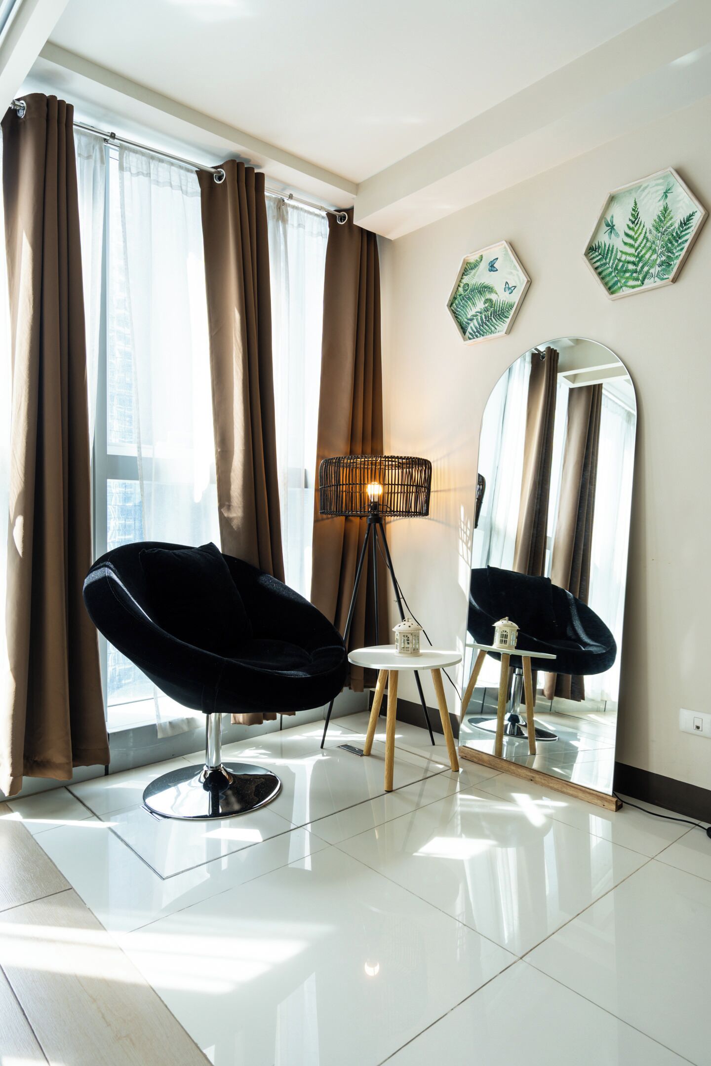 Un salon moderne avec un fauteuil noir, une lampe sur pied et un miroir au mur.
