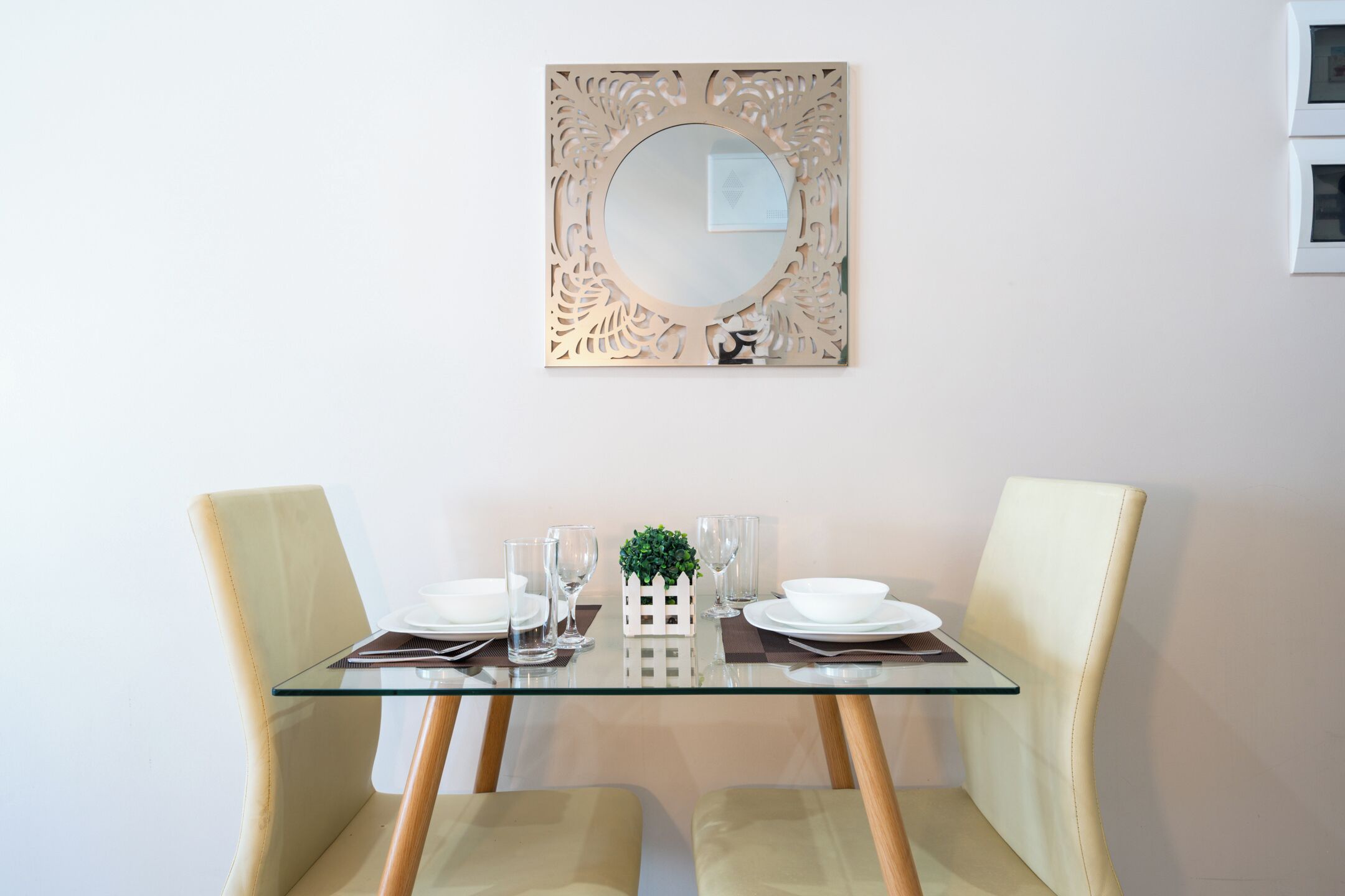 Une table à manger avec des chaises, un plateau en verre et un miroir décoratif placé au-dessus.