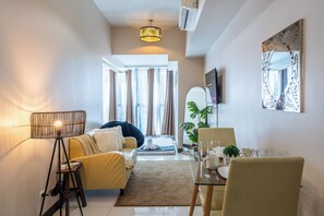 Ein modernes Wohnzimmer mit einer Couch, einem Couchtisch, einem Esstisch für zwei Personen und einem an der Wand befestigten Fernseher.