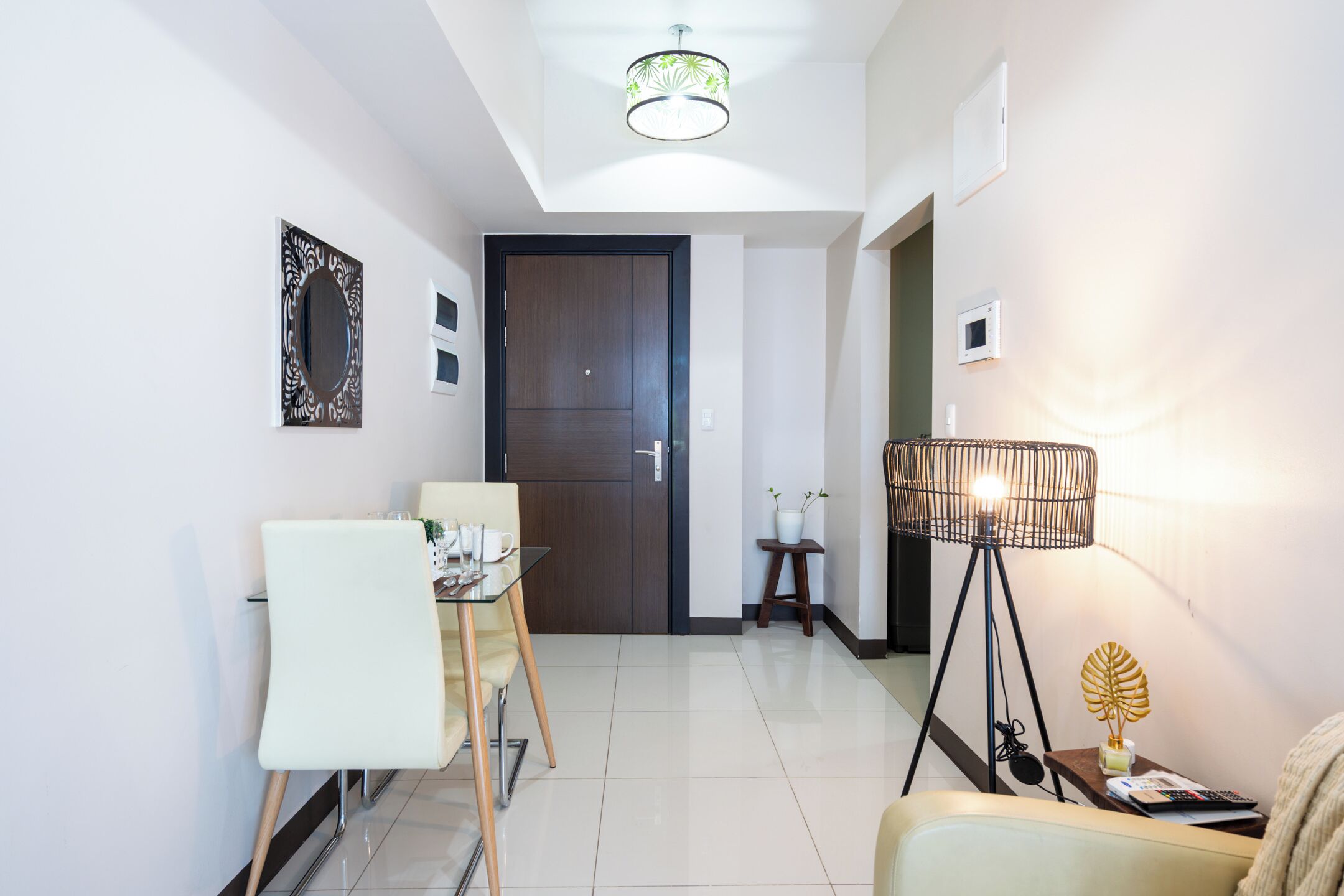 A modern living room with a dining area, a wooden door, a floor lamp, and a small table with a plant.