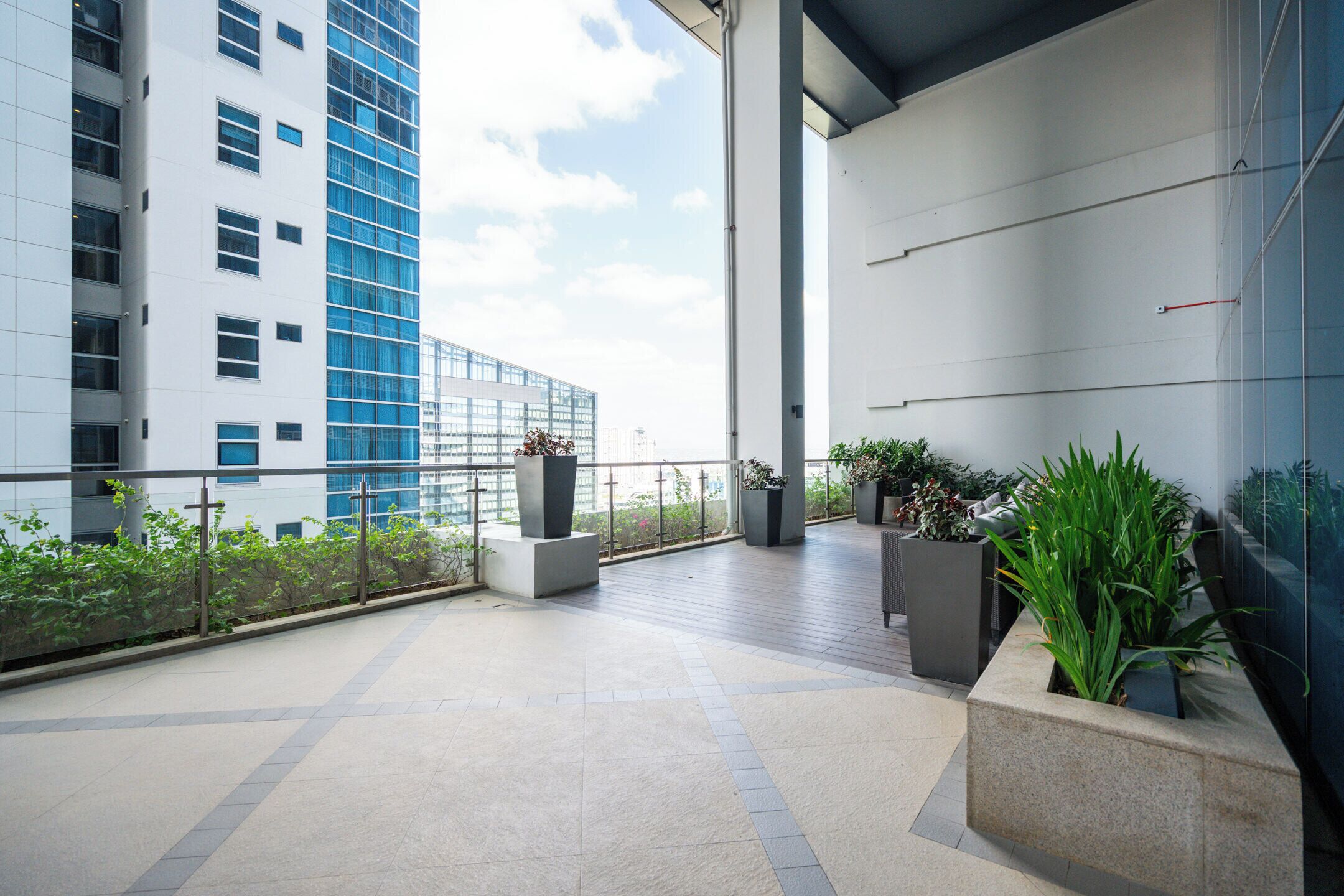 Une vaste terrasse extérieure au design moderne, comprenant un espace salon avec un canapé et plusieurs jardinières agrémentées de plantes vertes.