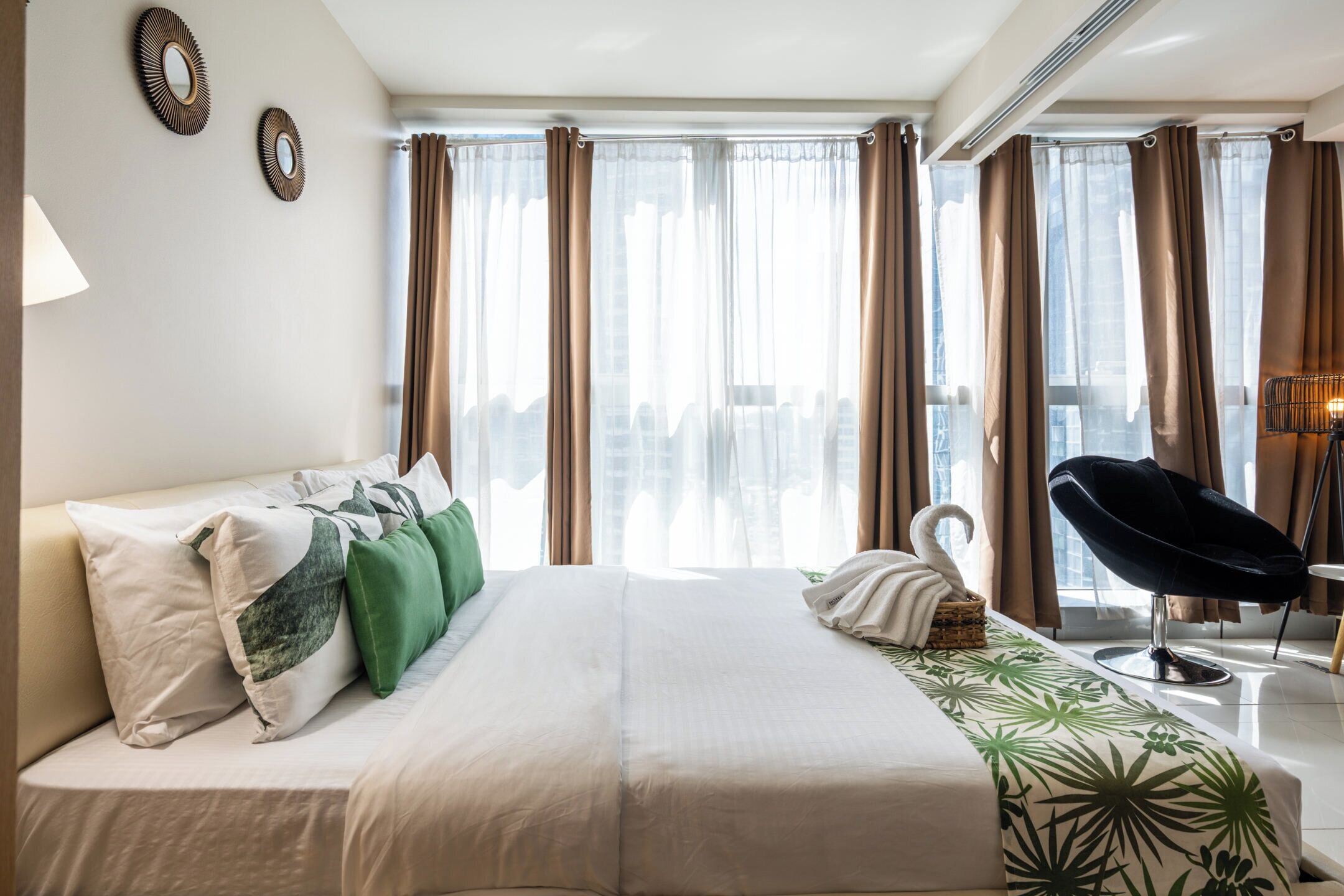 A hotel room with a bed, a chair, a lamp, and curtains.