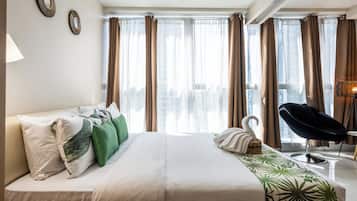 A hotel room with a bed, a chair, a lamp, and curtains.