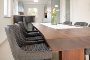 Un comedor moderno con una larga mesa de madera, sillas tapizadas en gris y un jarrón con flores sobre la mesa.