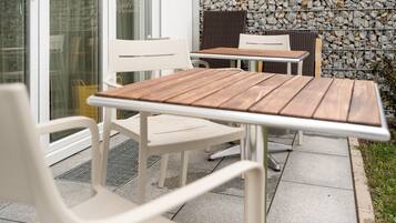 An outdoor seating area with white chairs and tables, a stone wall, and a glass door.