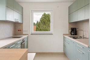 Una cocina moderna con armarios azul claro, una ventana con vistas a árboles, una cafetera y un lavamanos.