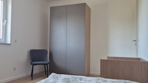 A room with a wardrobe, a chair, and a bed.
