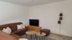A modern living room with a brown leather sofa, a flat-screen TV, a wooden coffee table, and a floor lamp. - Holiday Home 'Gästehaus Klosterblick' with Shared Terrace and Private Garden (Mainburg)