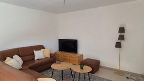 Ein modernes Wohnzimmer mit einem braunen Ledersofa, einem Flachbildfernseher, einem Holztisch und einer Stehlampe.
