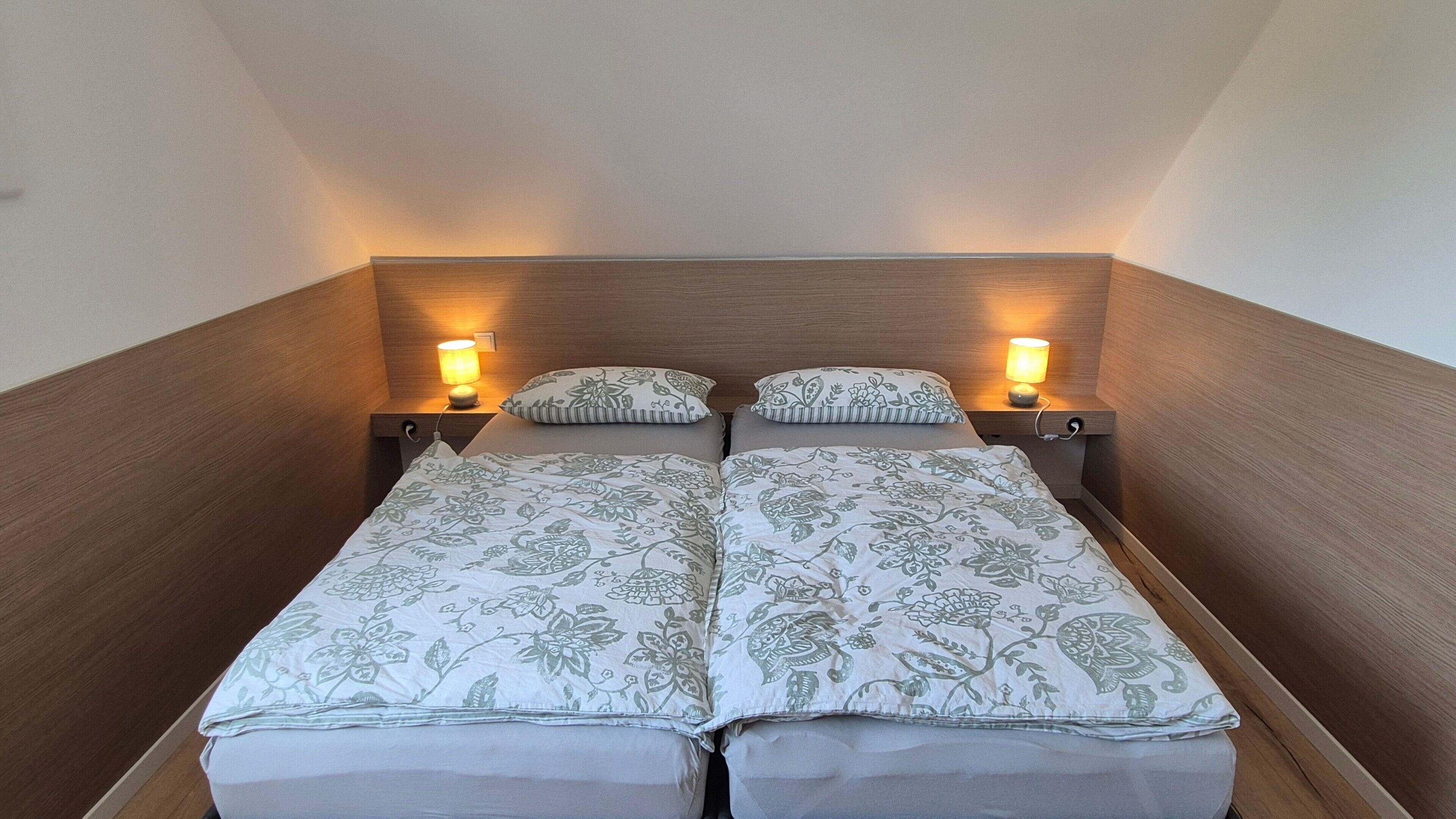 Ein Doppelbett mit floralem Bettbezug, zwei Nachttischlampen und ein hölzernes Kopfstück.