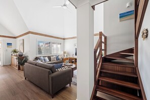 A spacious living room with a large sofa, a wooden staircase, and a view of the outdoors. - Clearwater Coastal: luxury beachfront getaway, walk to town (Dunsborough)