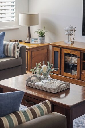 A living room with a sofa, a coffee table with a decorative tray, a lamp, and a cabinet with glass doors. - Clearwater Coastal: luxury beachfront getaway, walk to town (Dunsborough)