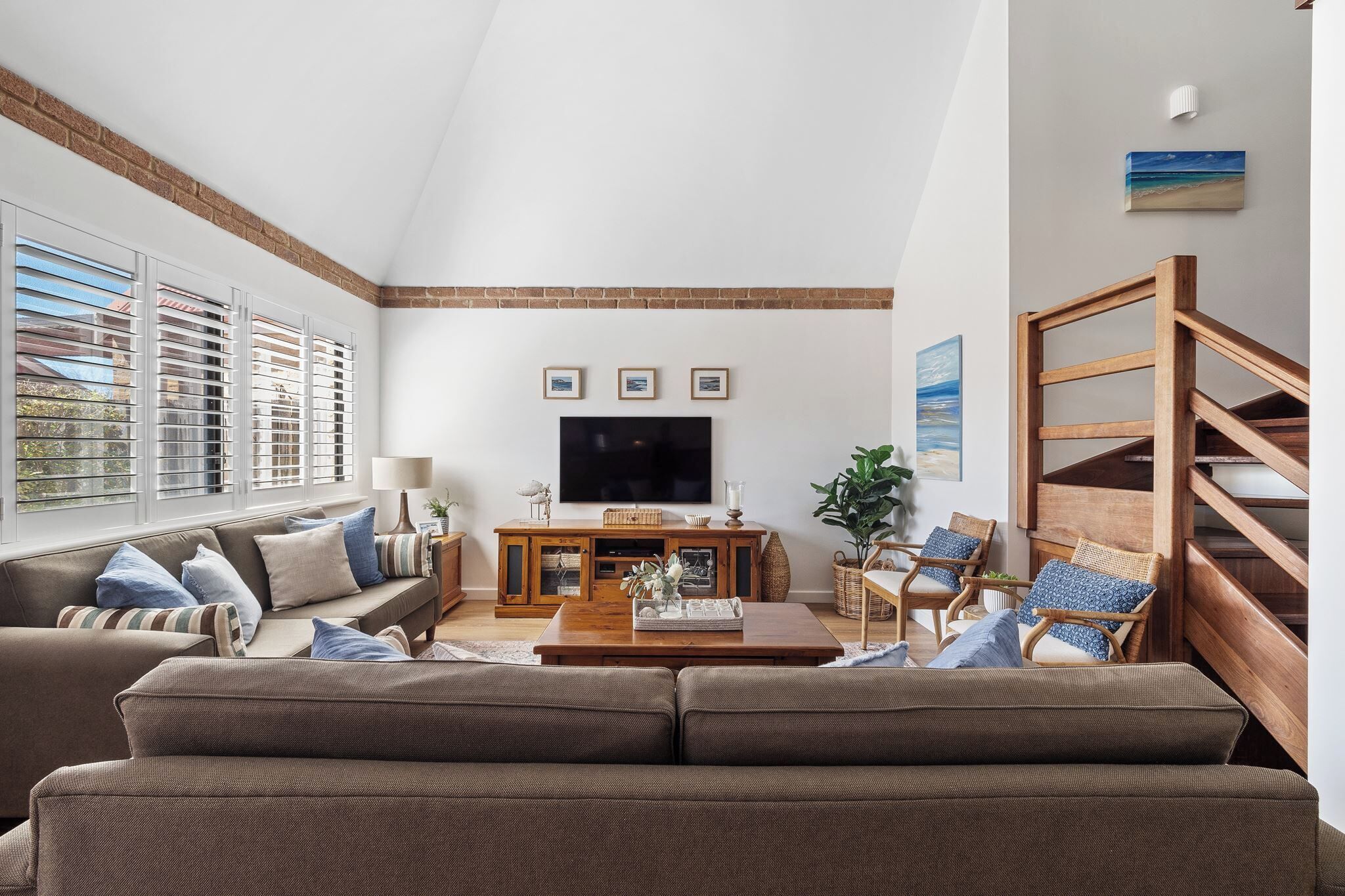 Una sala de estar con un ventanal grande, un televisor de pantalla plana, una mesa de centro de madera y una escalera.