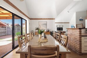 A spacious dining area with a long table, wooden chairs, and a brick accent wall. - Clearwater Coastal: luxury beachfront getaway, walk to town (Dunsborough)