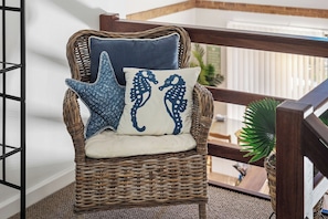 A wicker chair with a cushion and two decorative pillows, one with a seahorse design and another with a starfish pattern, positioned in a room with a view of a balcony. - Clearwater Coastal: luxury beachfront getaway, walk to town (Dunsborough)
