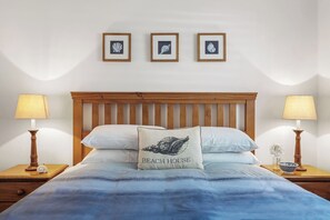 A bedroom with a wooden headboard, a bed with blue bedding, two bedside lamps, and three framed pictures on the wall. - Clearwater Coastal: luxury beachfront getaway, walk to town (Dunsborough)