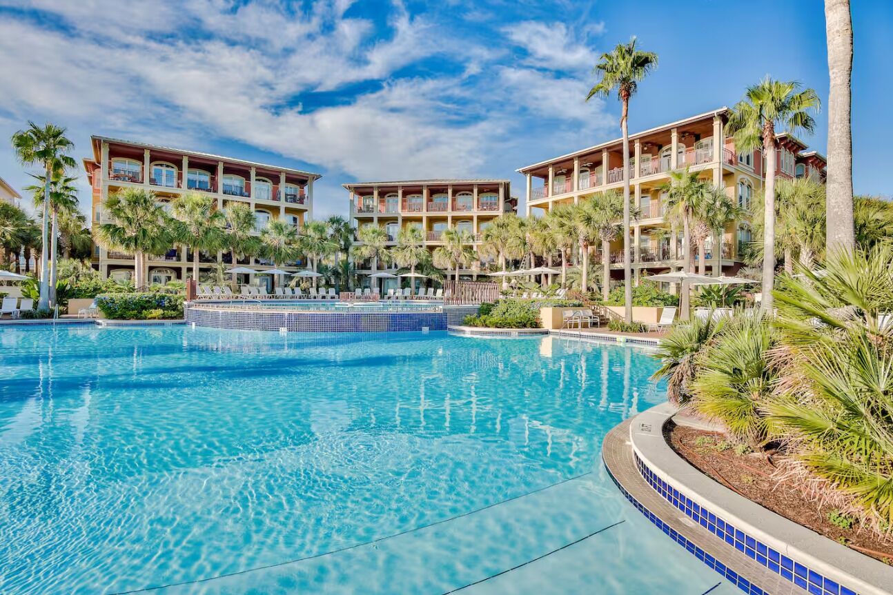 Een resort met een groot zwembad, omgeven door palmbomen en meerlaagsgebouwen.