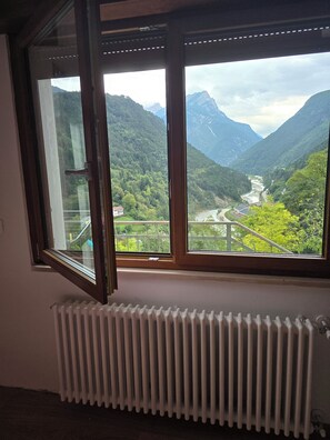 A room with a large window overlooking a mountainous landscape with a river and buildings.