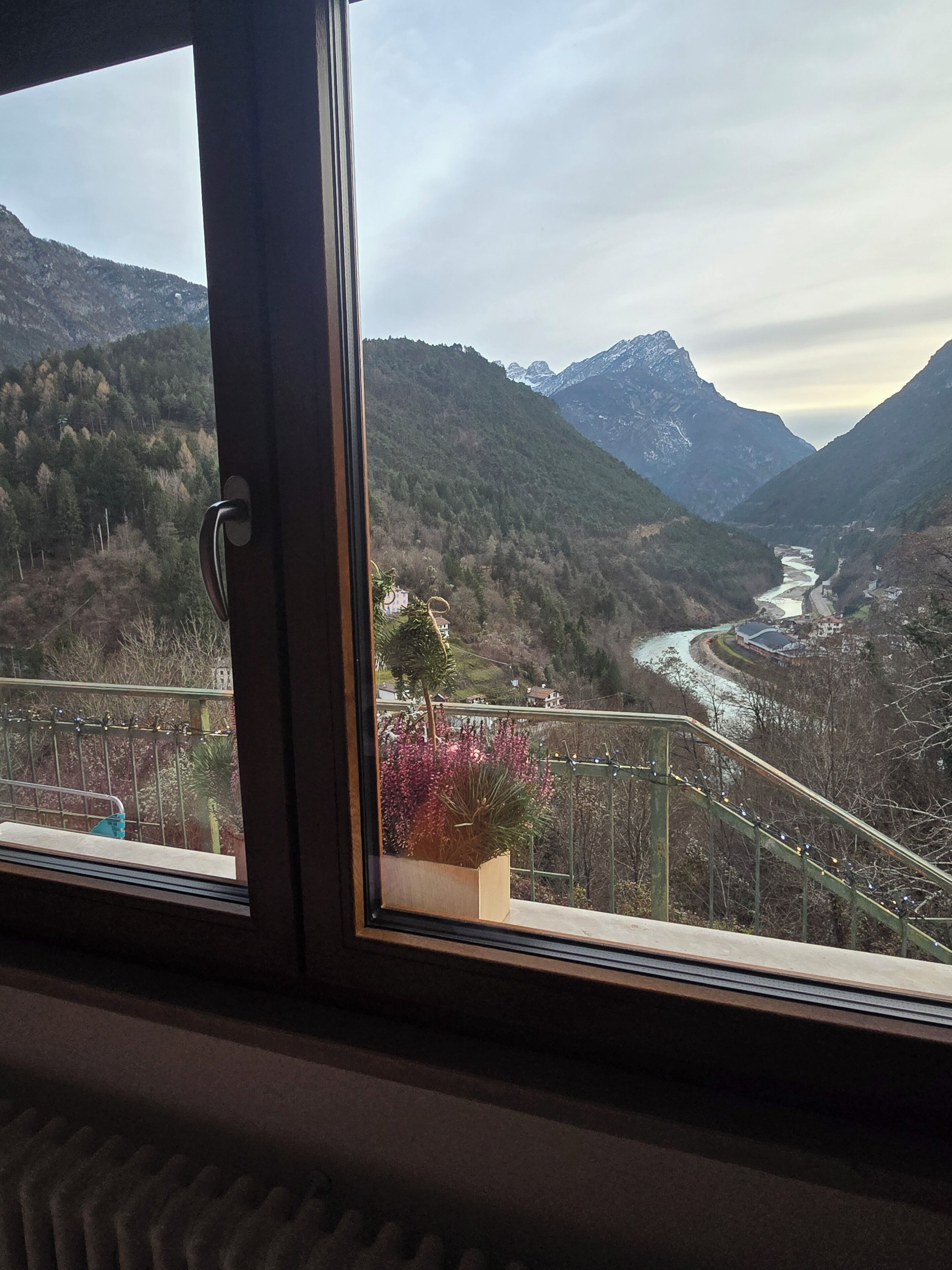 A window view of a mountainous landscape with a river, a bridge, and a railing.