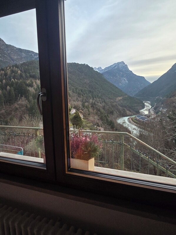 A window view of a mountainous landscape with a river, a bridge, and a railing.