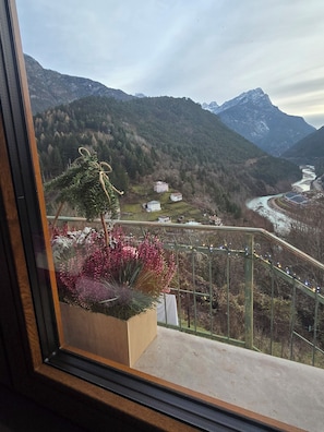 Uma varanda com vista para um rio, montanhas e um jardim florido.