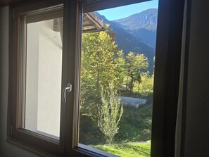 Uma janela com vista para uma paisagem montanhosa e uma árvore.