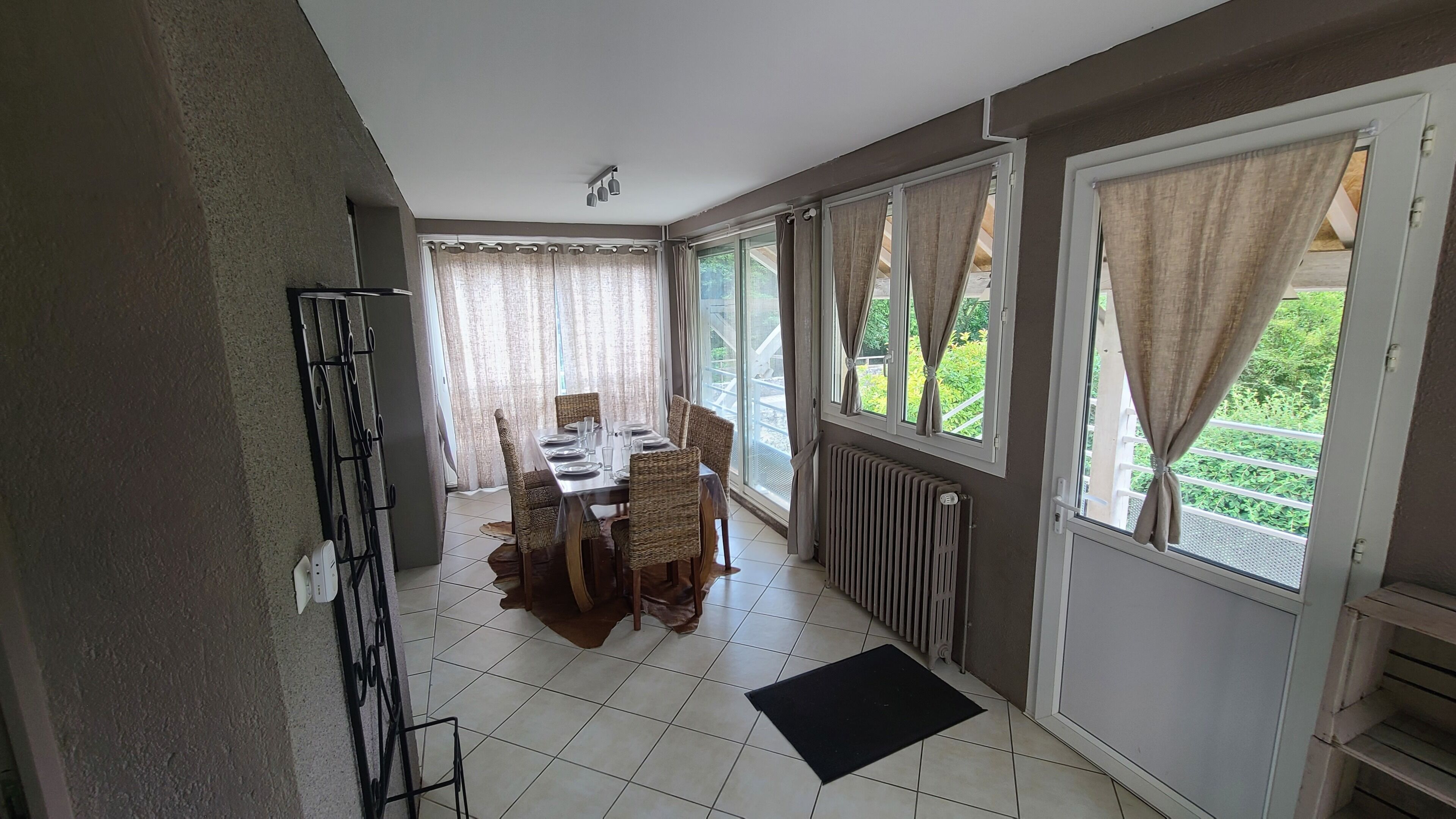 A dining area with a table set for four, a radiator, and a view of greenery through the windows.