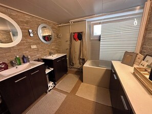 Ett modernt badrum med två handfat, ett badkar och en dusch. Handdukar och hygienartiklar finns på bänken.