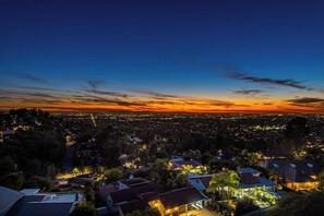 A cityscape at dusk with illuminated buildings and a sunset.