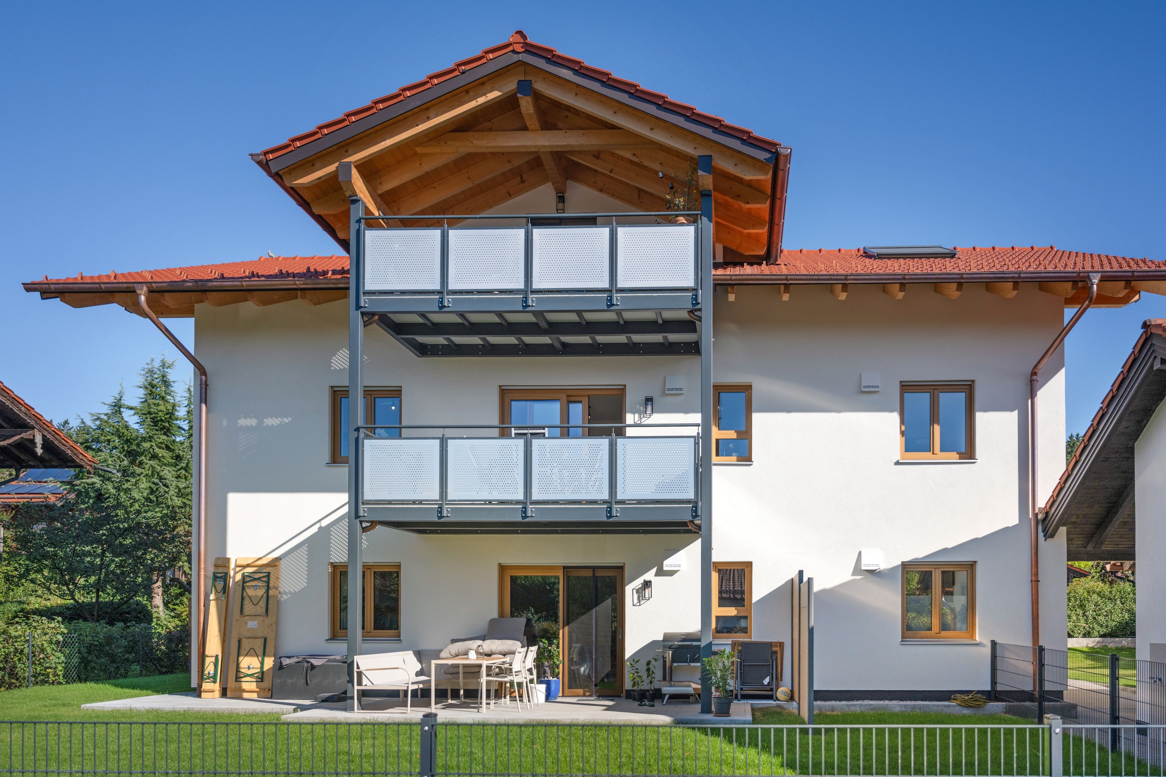 Ein zweistöckiges Haus mit Balkon, überdachter Terrasse und umzäunter Hof.