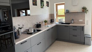 A modern kitchen with grey cabinets, a black refrigerator, a sink, and a window with a view of greenery.