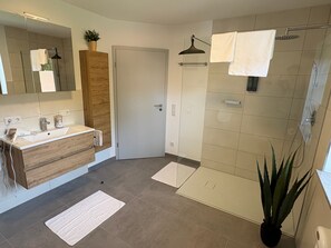 Un bagno moderno con un mobile bagno in legno, uno spazio doccia in vetro e una pianta in vaso.