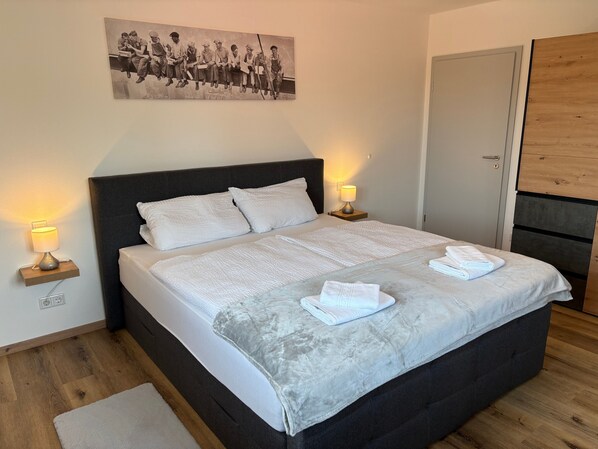 A bedroom with a large bed, two bedside lamps, a wooden headboard, a door, and a framed picture on the wall.