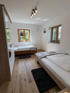 Una camera da letto con due letti, pavimento in legno, una finestra con vista e una lampada a soffitto.
