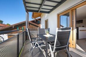 Un balcon avec une table et des chaises, une porte en bois et une vue sur les bâtiments voisins.